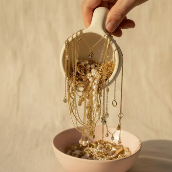 Mystery jewelry scoop bowl with gold and pearl fashion jewelry in warm natural light